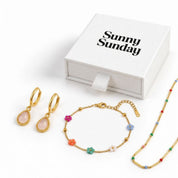 A jewelry set from Sunny Sunday on a white background, featuring gold hoop earrings with pink stones, a gold beaded bracelet, and a gold beaded necklace, next to a white gift box.