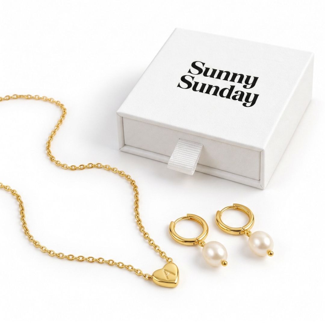 Gold jewelry set with a heart-shaped pendant necklace, matching hoop earrings with pearl drops, and a white gift box printed with the brand name 'Sunny Sunday'.