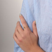 A close-up of a person wearing a light blue linen button-up shirt, with one hand resting on the chest and a gold ring visible on the finger.