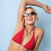 A woman wearing a red halter bikini top with small white polka dots and blue denim shorts, posing against a solid light blue background.