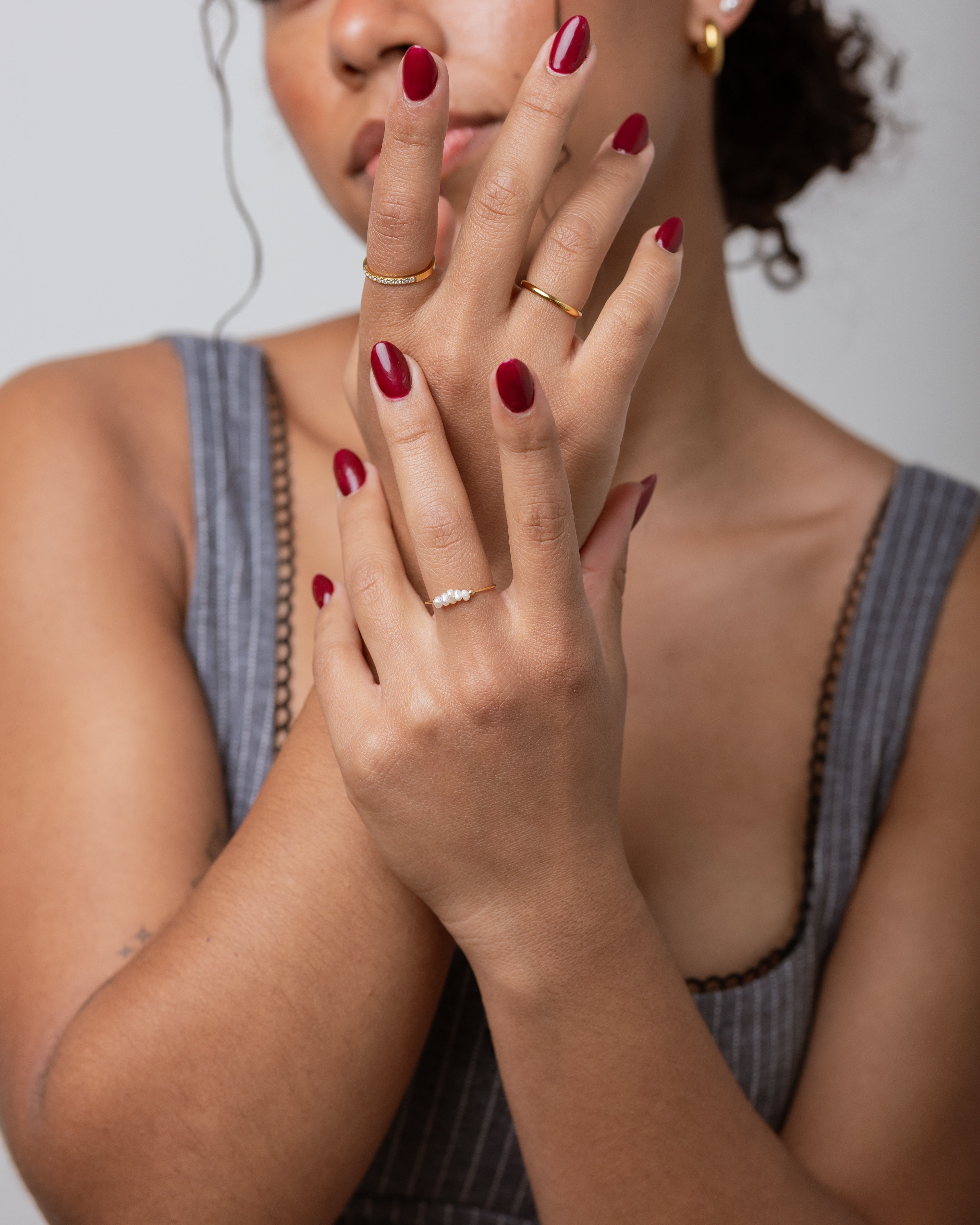 Woman with red nail polish and a ring, wearing a gray sleeveless top.