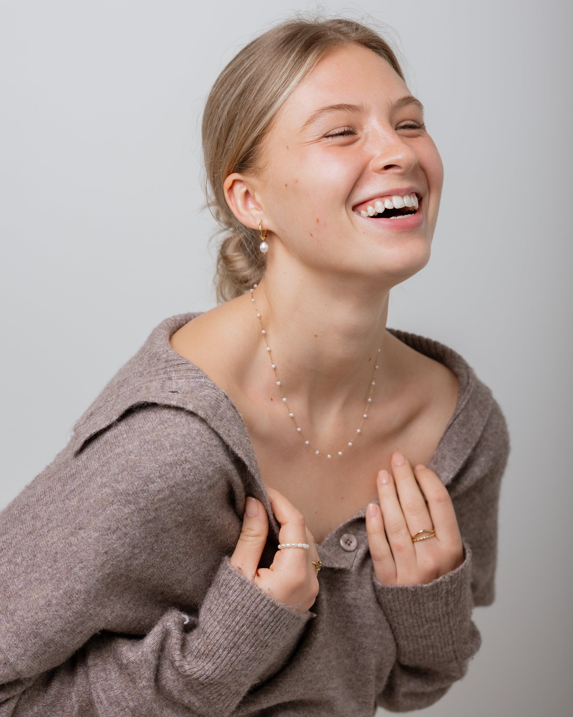 Woman wearing a brown sweater and necklace, smiling against a plain background