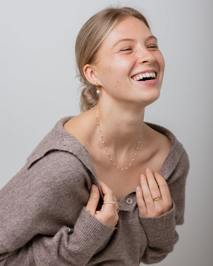 Woman wearing a brown sweater and necklace, smiling against a plain background