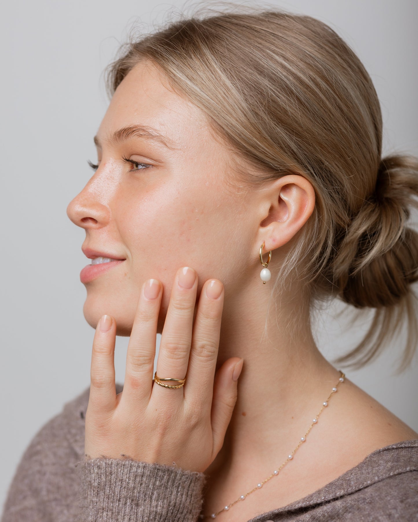 Woman wearing earrings and a ring, with a neutral background