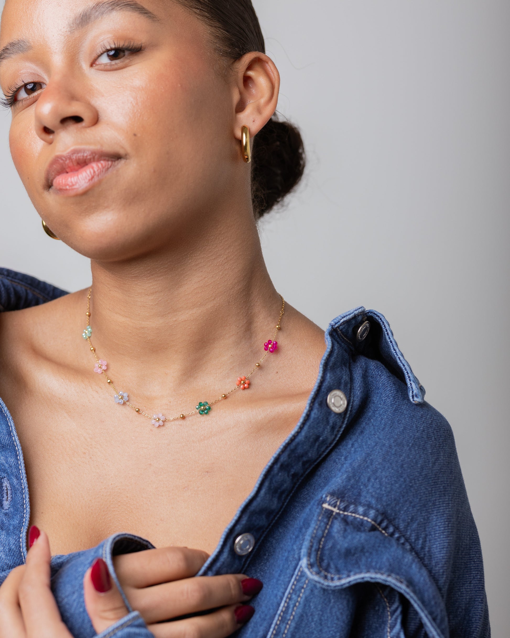 Woman wearing a colorful necklace with a denim jacket on a plain background