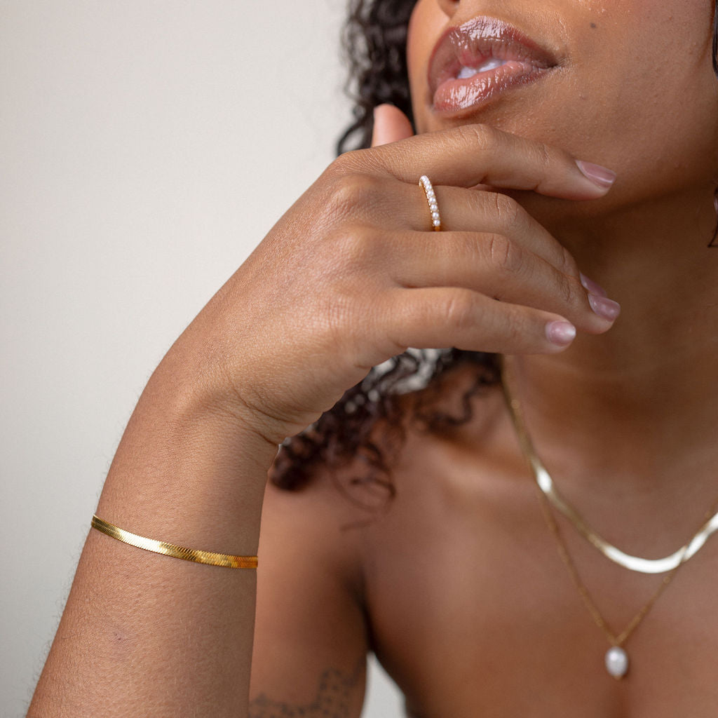Woman wearing gold jewelry including a bracelet, ring, and necklace against a neutral background