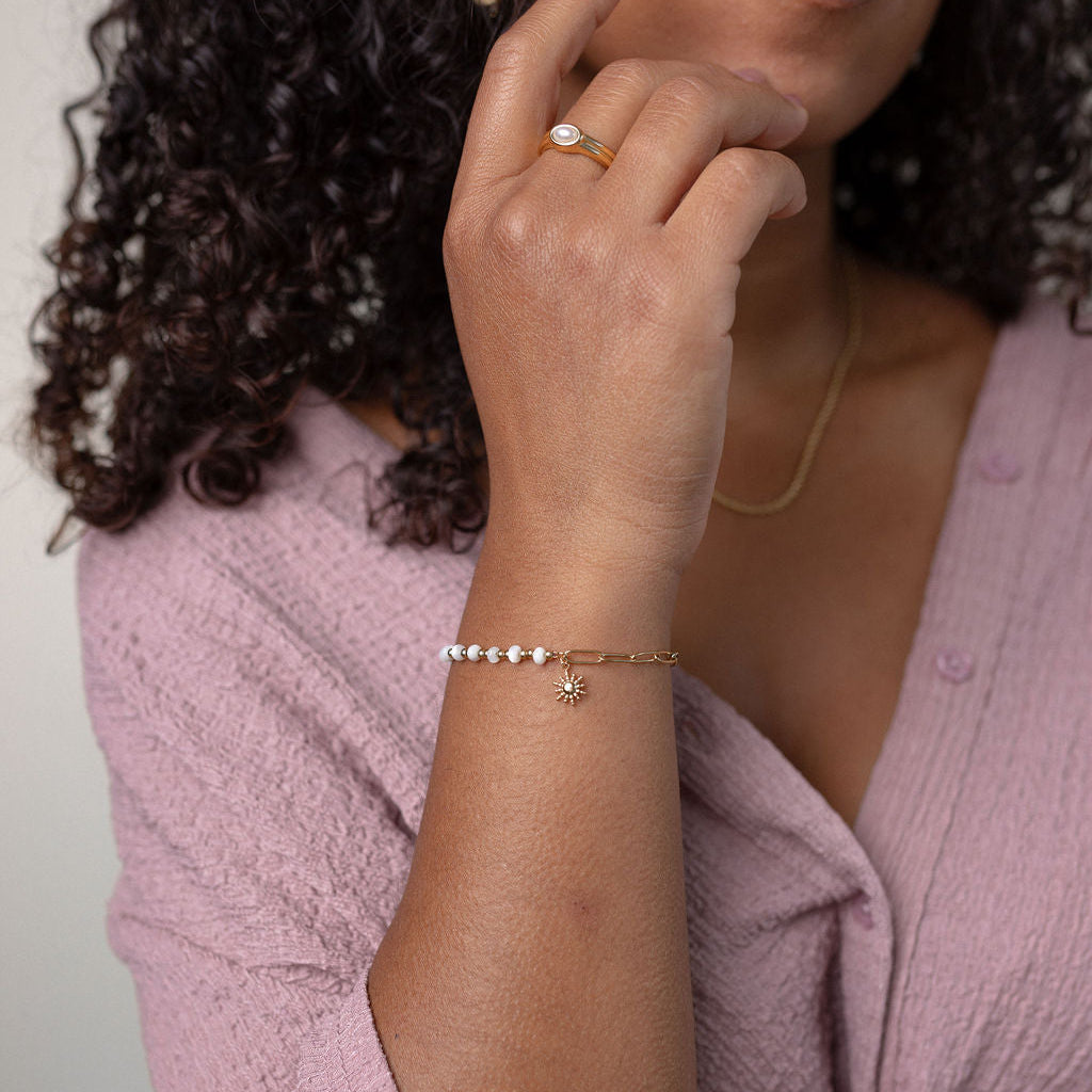 Woman wearing a pink textured top with jewelry on a neutral background
