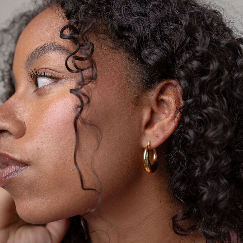 Woman with curly hair wearing a pink sweater and gold earring.