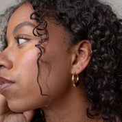 Woman with curly hair wearing a pink sweater and gold earring.