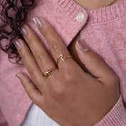 Hand wearing gold rings with a pink sweater background